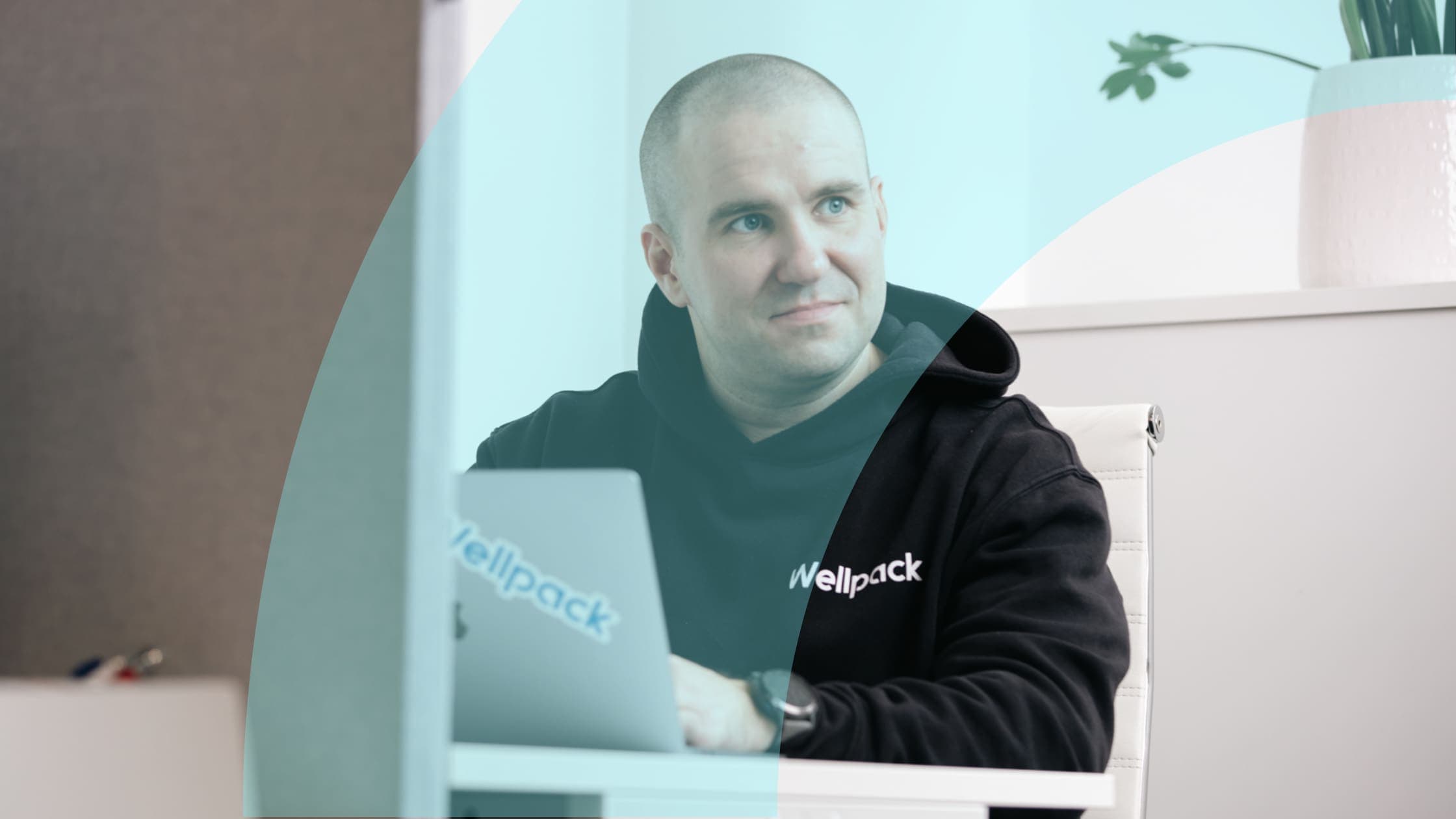Wellpack-huppariin pukeutunut työntekijä kannettavan tietokoneen ääressä toimistossa.