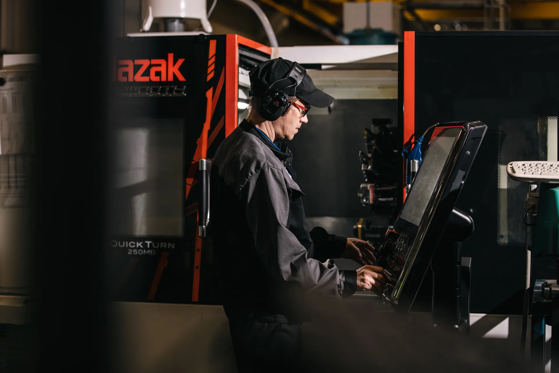 Machinist at a CNC lathe control panel, ear defenders and safety glasses