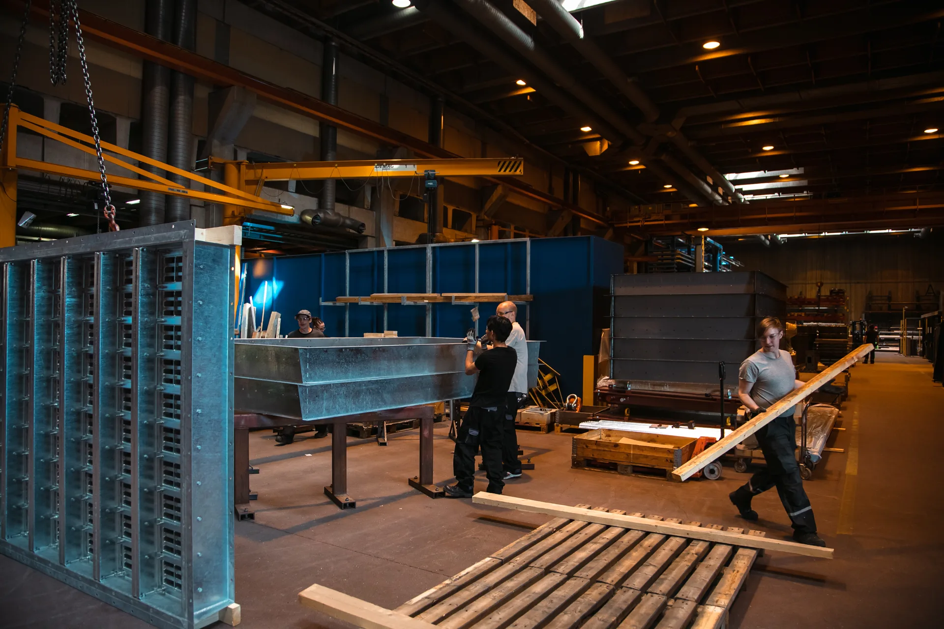 Workers assembling steel structures in a hall, overhead crane above