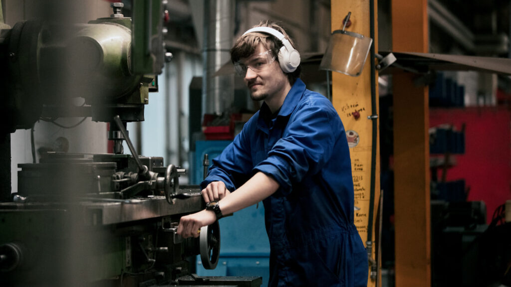 Nuori Sisu Auton työntekijä, joka hymyilee kameralle tai työskentelee ajoneuvon parissa Karjaan tehtaalla.